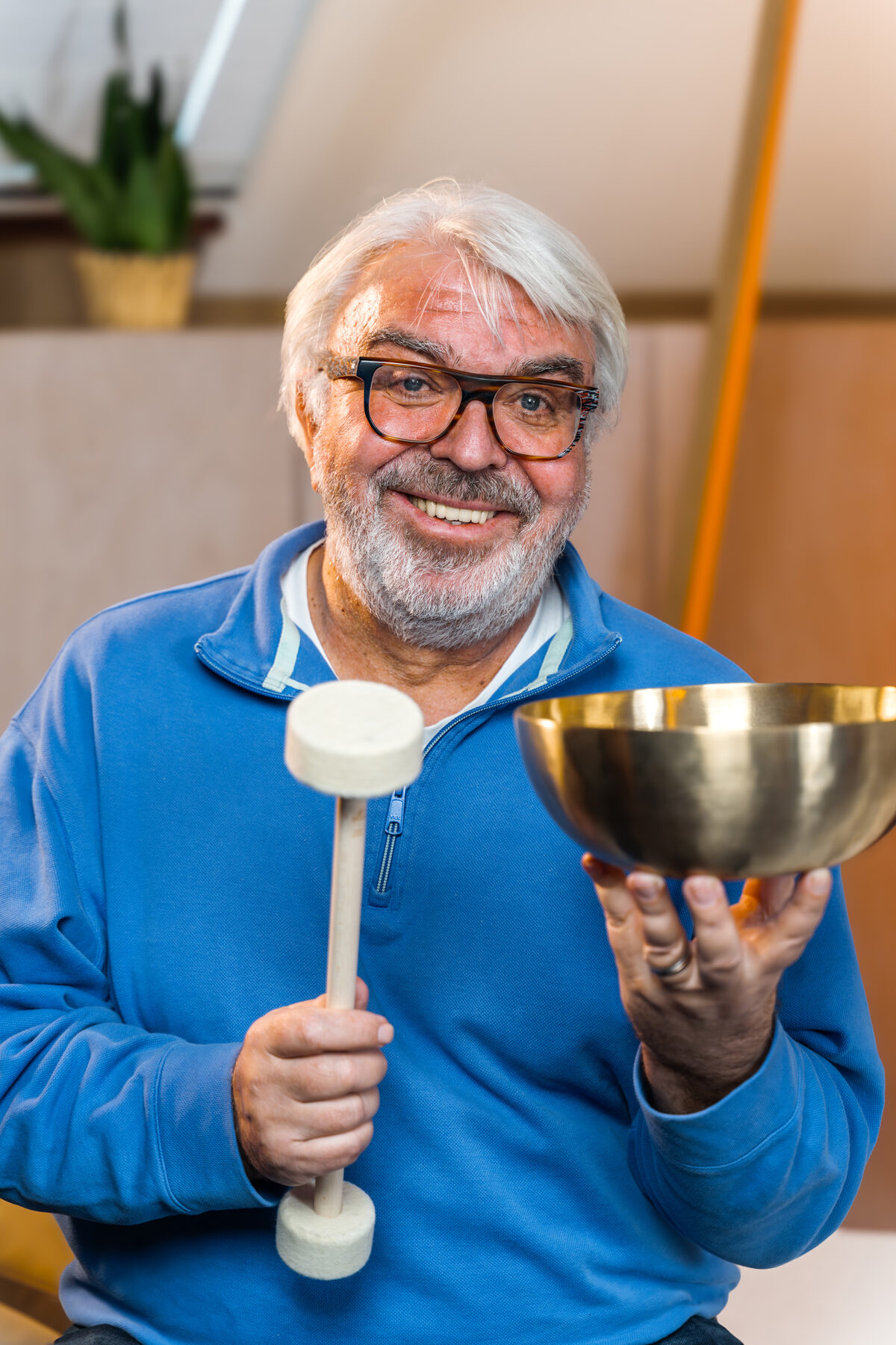 Norbert Kasprowski hält eine Klangschale und einen Filzschlägel in den Händen und lächelt in die Kamera.